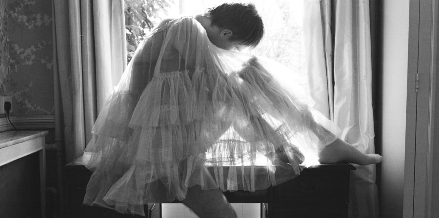 Black and white photograph of a dancer, folded, by a window.