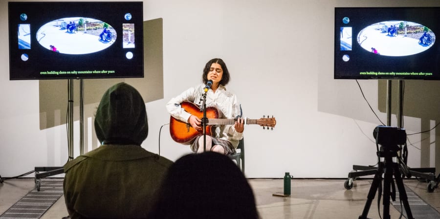 woman with guitar and two screens behind her