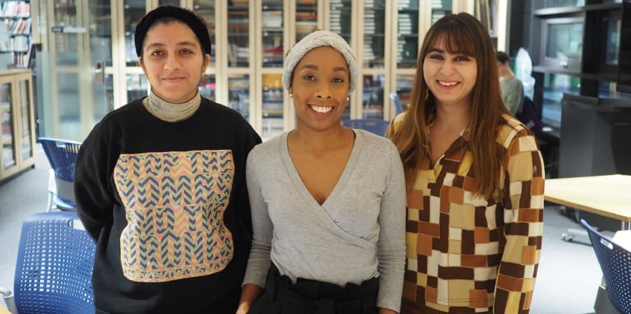 three woman stand in a line smiling at the camera, and office our of focus behind them