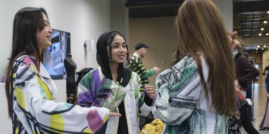 3 students stand together talking in their vibrantly printed garments that they made at the Saturday Club