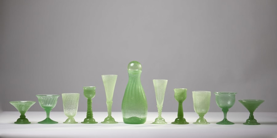 Green glassware of different heights stand on a white tablecloth