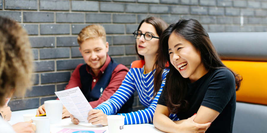 One female student laughing, sitting with 3 other students in a booth with books and papers on table