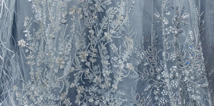 Detail of a costume by Yuyuan Wei. It is blue tulle with beads and sequins sewn on in a flower design.