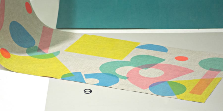 screen printed fabric with coloured circles lay on colour sheets in a window
