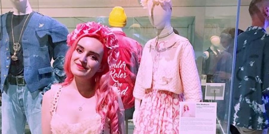 Young project team volunteer Ellie Medhurst in pink standing in front of mannequin dressed in her clothes donated to Queer Looks exhibition, Brighton Museum, 2018-19.