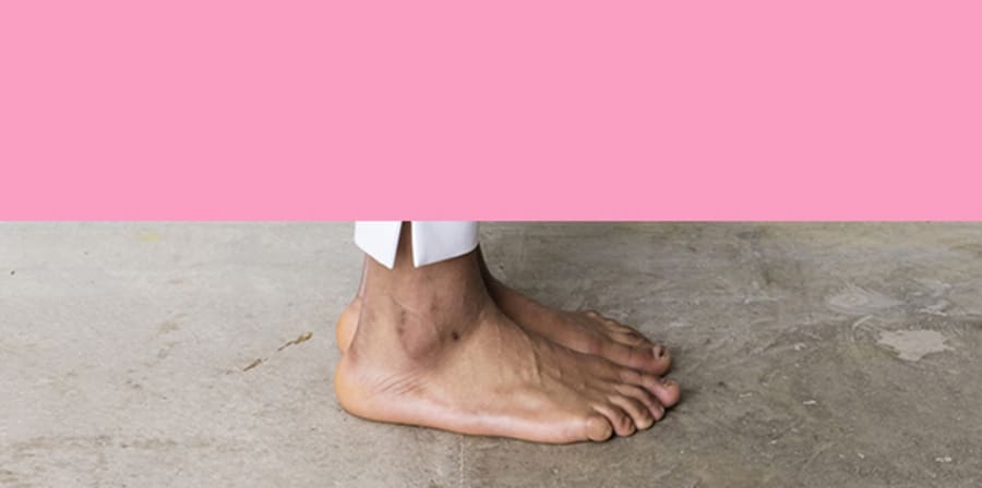 Photograph of a foot stood on concrete with a pink background