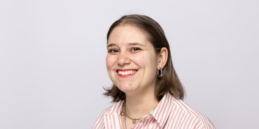 A headshot of Chiara Carnevale, she smiles at the camera wearing a salmon stripped shirt, gold necklaces and silver earrings.