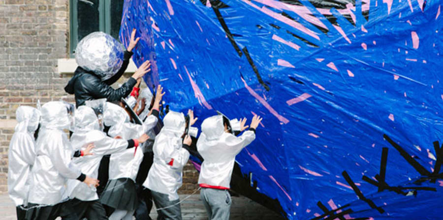 Children in white boiler suits pushing large blue ball