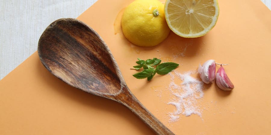 A wooden chopping board covered with a wooden spoon, herbs and half a lemon.