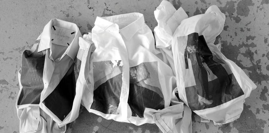 Black and white photograph of three folded shirts on a concrete background