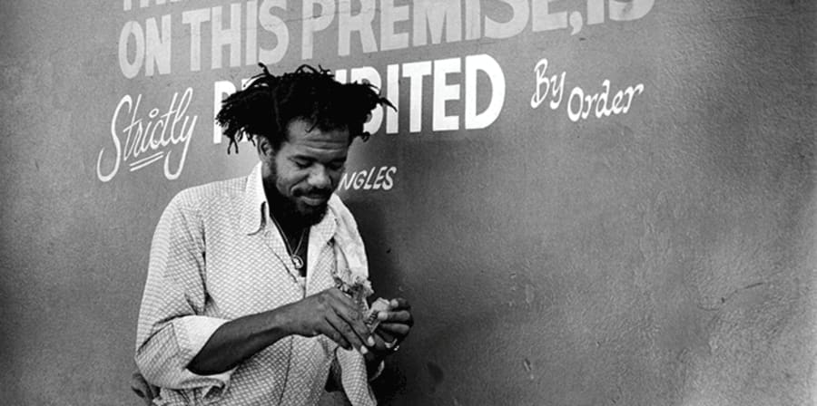 Black and white photograph of signer Glen Brown smoking in front of a handwritten no smoking sign 