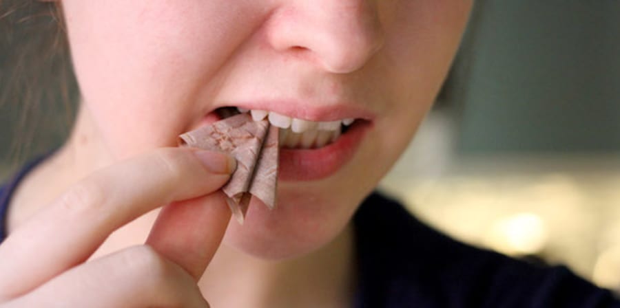 Close-up photograph of a piece of folded paper in-between a person's teeth