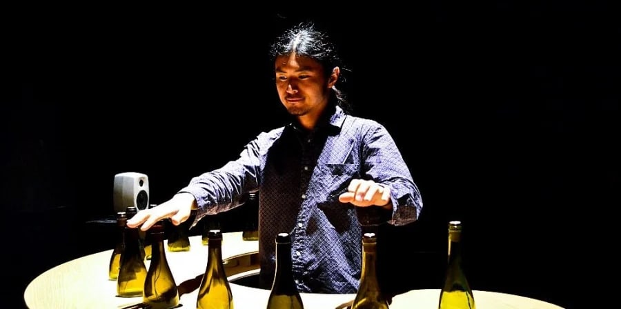 An arrangement of bottles designed to produced music with a man standing behind it.