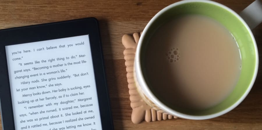 Photo of a Kindle displaying a page from an e-book, resting on a table top alongside a mug of tea