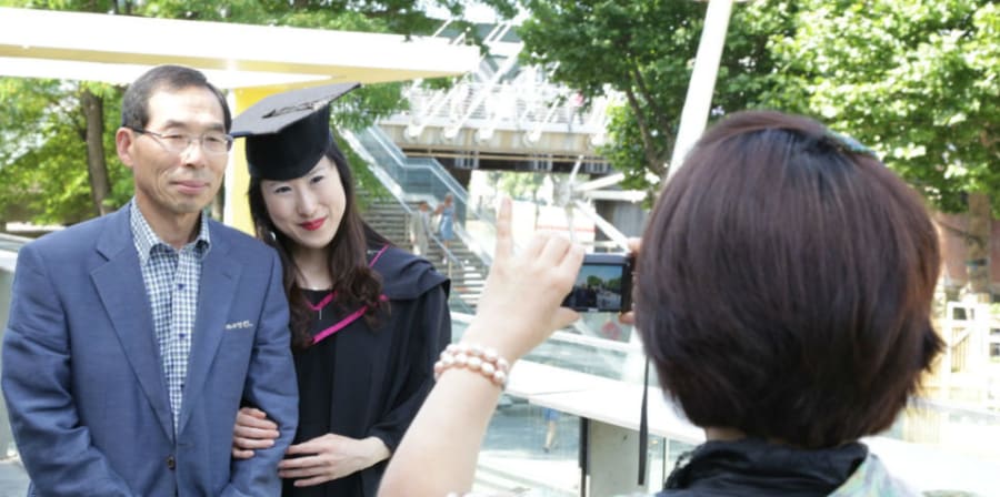 A graduate in their graduation gown having a photo taken with their parents.