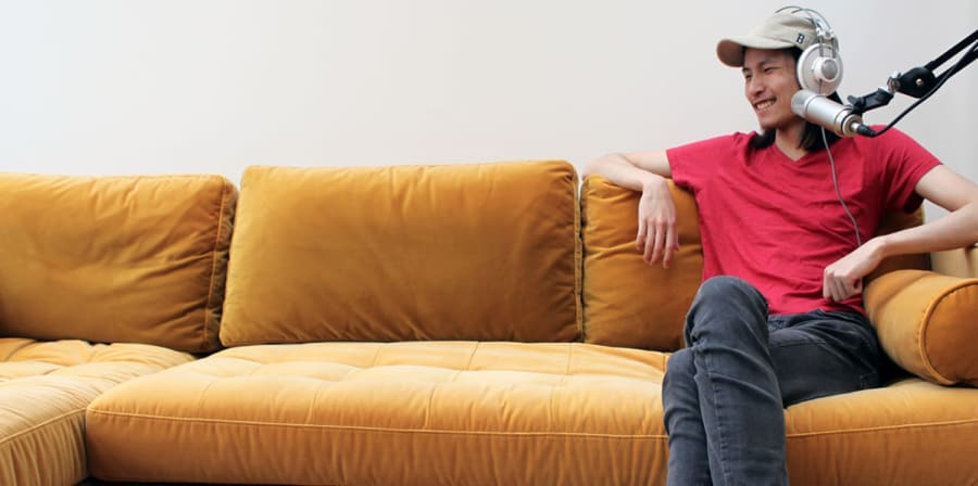 Justin sits beside a microphone on a yellow sofa.