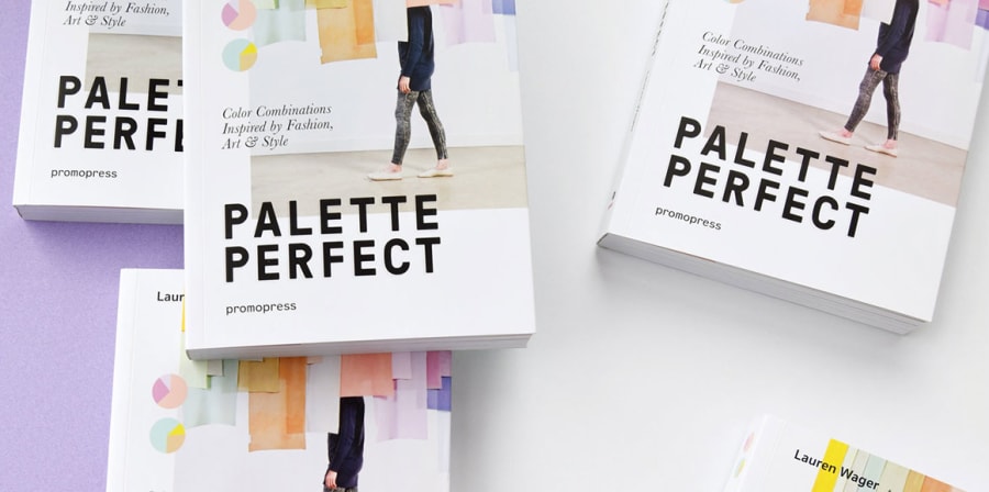 An arrangement of copies of Palette Perfect, the covers of which feature a single figure walking across a gallery space filled with hanging colour banners.