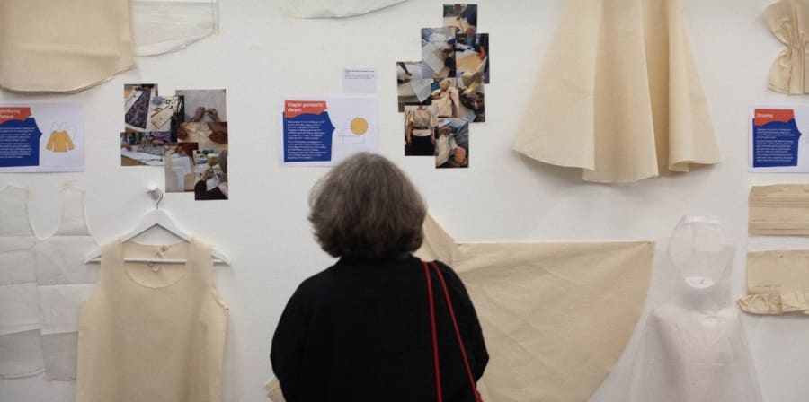 a back view of a woman looking at an exhibition of cut out garment pieces