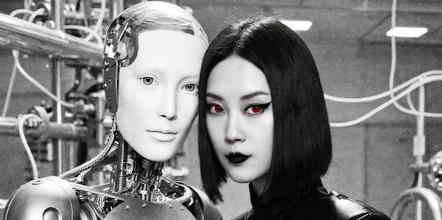 Black and white portrait of a person standing beside a humanoid robot in a laboratory setting.