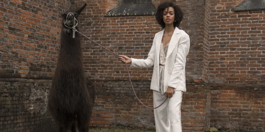 Photograph of female model in a white suit with an alpaca