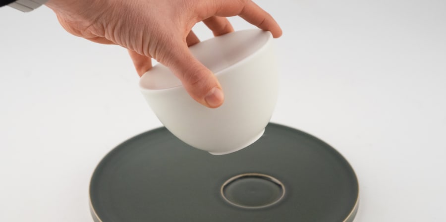 hand is picking up a cup from a saucer on a white backdrop