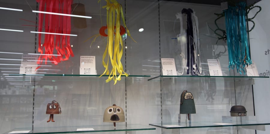 Exhibition display cabinet with 4 objects with humorous faces, above which are a colourful decorative streamers.  2. Section of the new 