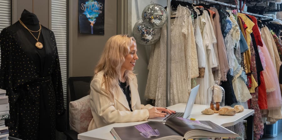 Person at a desk with rail of colourful dresses and disco balls behind.