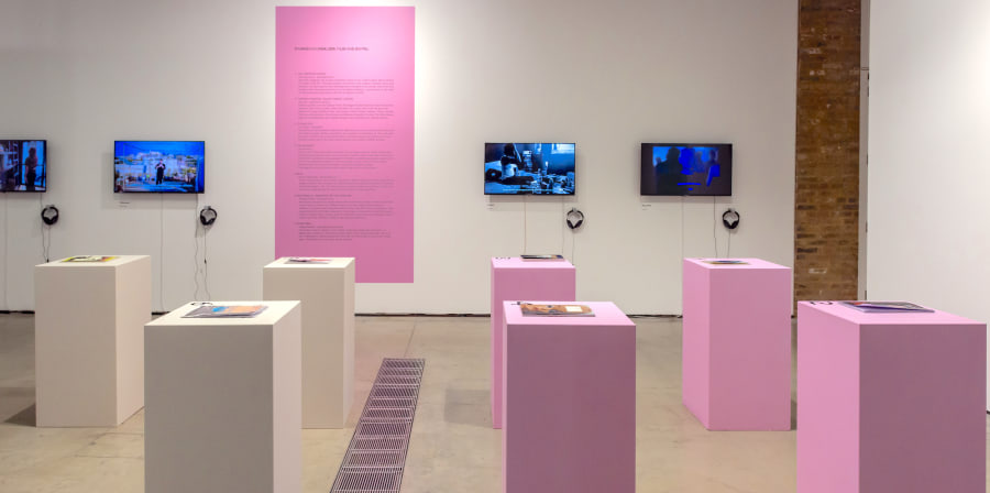 pink plinths with publications and tvs on the wall with headphones in the gallery