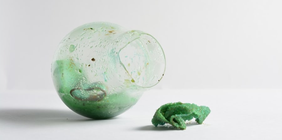 A smashed glass lightbulb with green oxidised crystals growing out of it