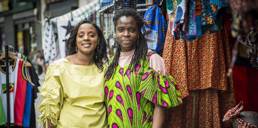 Image depicts two women standing in front of clothes styles as part of the It's Your Local Market project.