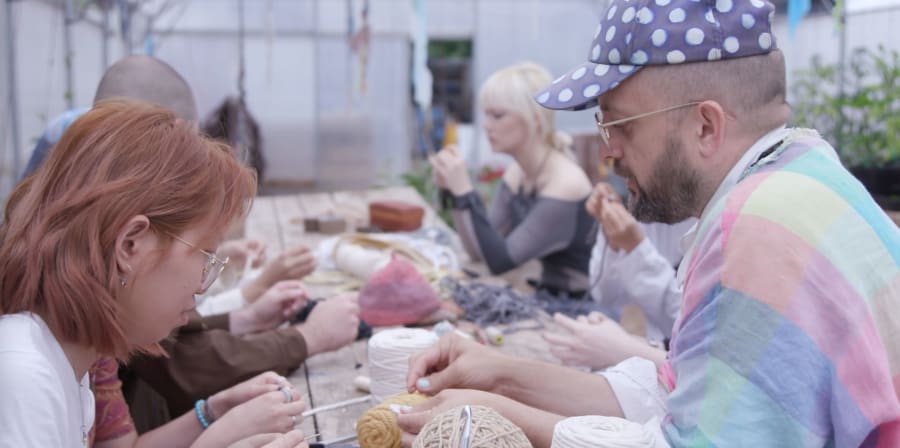 a man in a spotted hat is handling yarn with a girl on the other side of the table looking at it