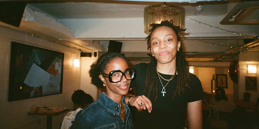 Two people standing together indoors at an event venue, with tables and warm lighting in the background.