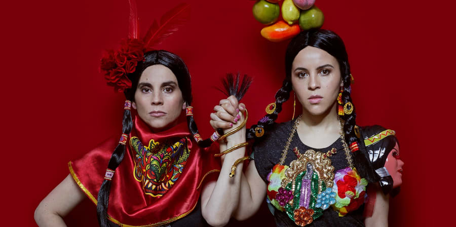 Two Latin American women standing together, holding hands in string pose.