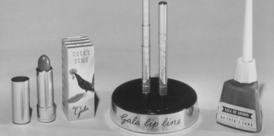 A black and white photo of cosmetics lined up, including lipstick, lip liner and nail polish from the 1950s.