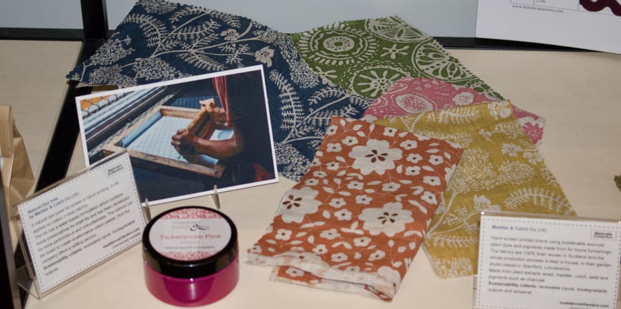 Photograph showing a section of a display featuring a jar of ink, colourful fabrics with floral patterns and a photograph of a person screenprinting
