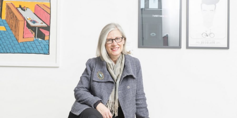 Photo of Sarah Atkinson sitting in a gallery and smiling.