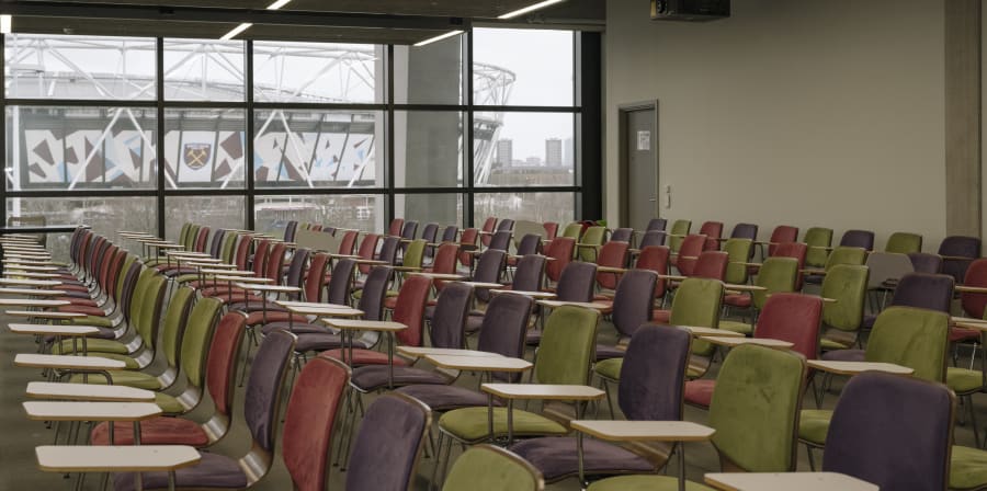 Rows of seats in a large room with a window overlooking a stadium in the background. 