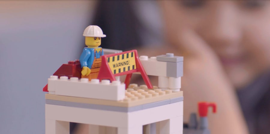 Close up still from a film. Lego tower with a lego construction worker.