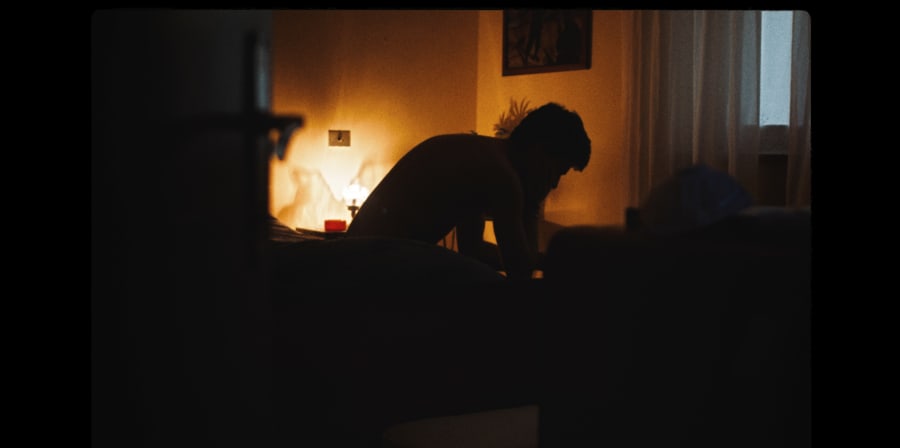 A silhouette of a boy sitting on a bed.