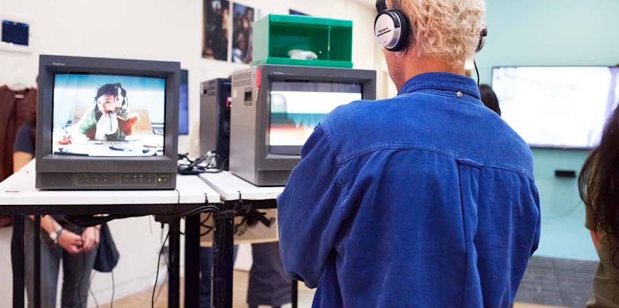 Student wearing headphones and looking at an animation on a small screen in a gallery.