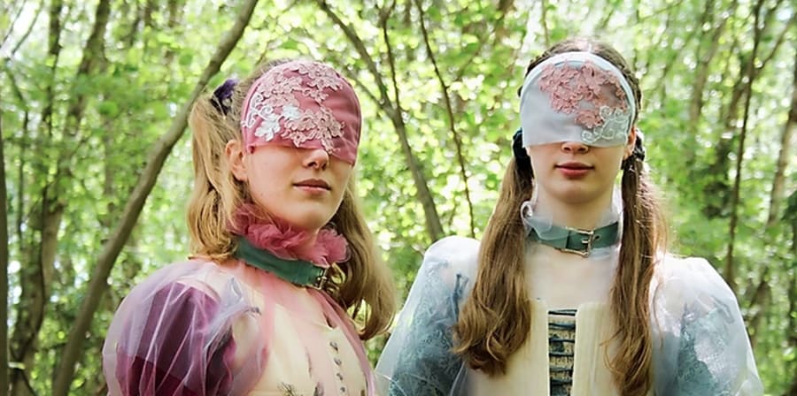 two masked models face the camera while in a forest looking away from the camera wearing garments inspired by the pre-Raphaelite art movement