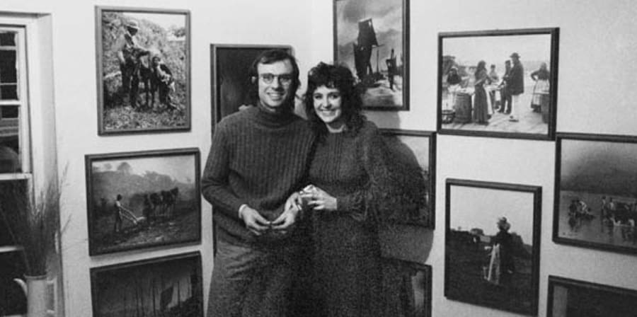 Two people standing in front of a wall of photographs 