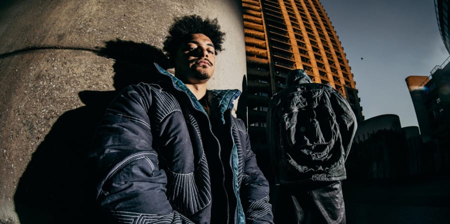 Model in puffer jacket leaning against industrial building.