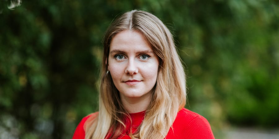 Woman in red standing in front of tree.