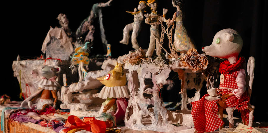 Table with various different puppets on it including bears wearing clothes and small human figures.