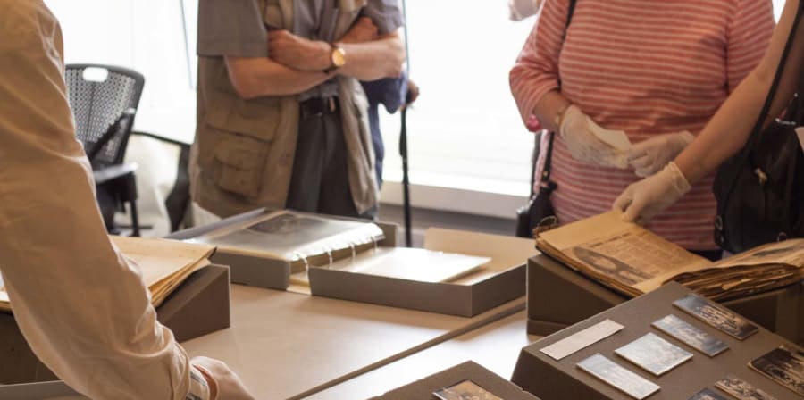 Colour photograph showing historic documents displayed on a table on foam wedge supports with people standing over them to look
