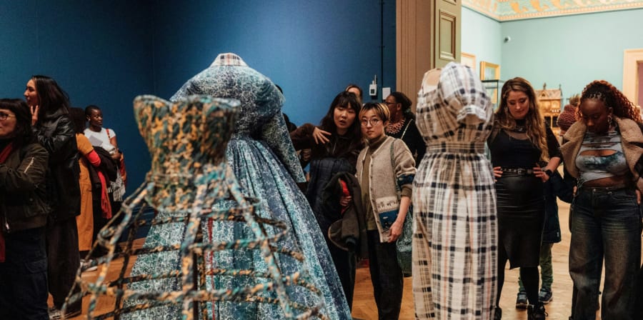 Visitors looking at dresses on mannequins at exhibition.