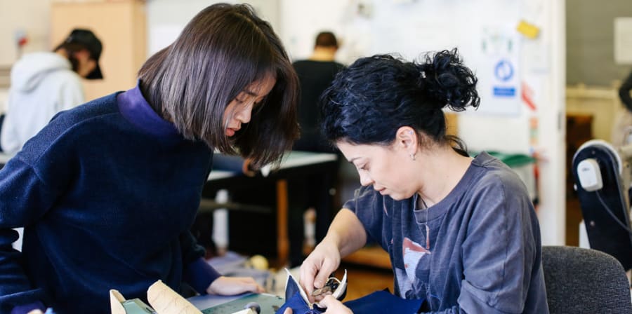 Two female students in a workshop leaning over a piece of work with tools in hand
