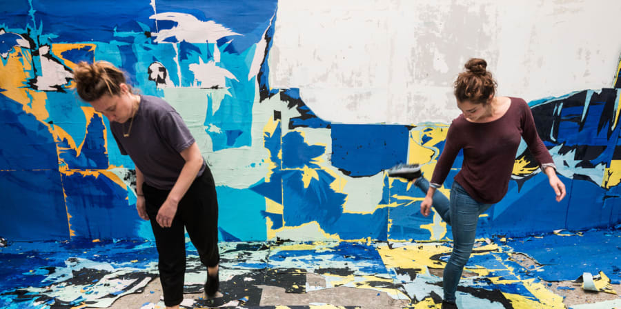 Two artists create work in a room covered in blue, yellow and white squares.