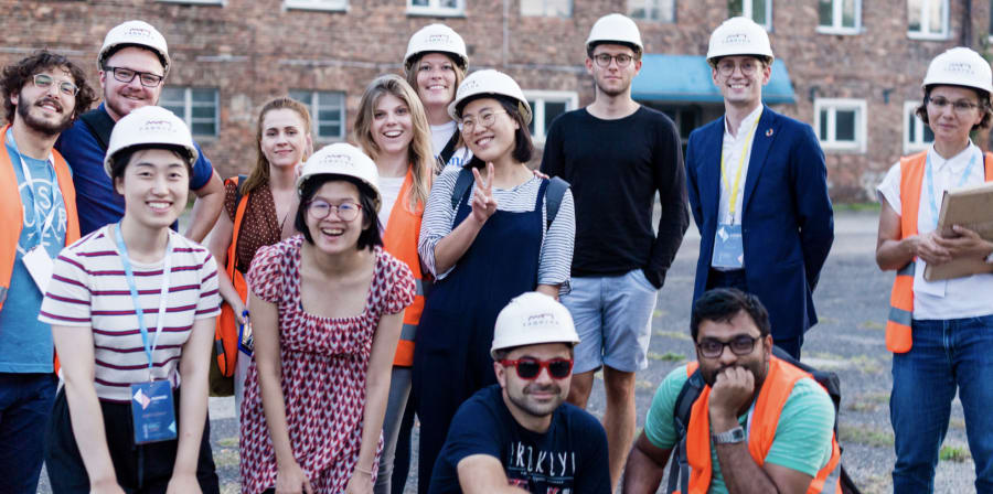 Group of students in front of a construction site wearing builders helmets